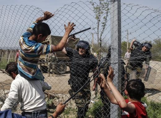 A Macedonian policeman uses his baton to prevent migrants and refugees to open the border fence at a makeshift camp at the Greek-Macedonian border near the village of Idomeni