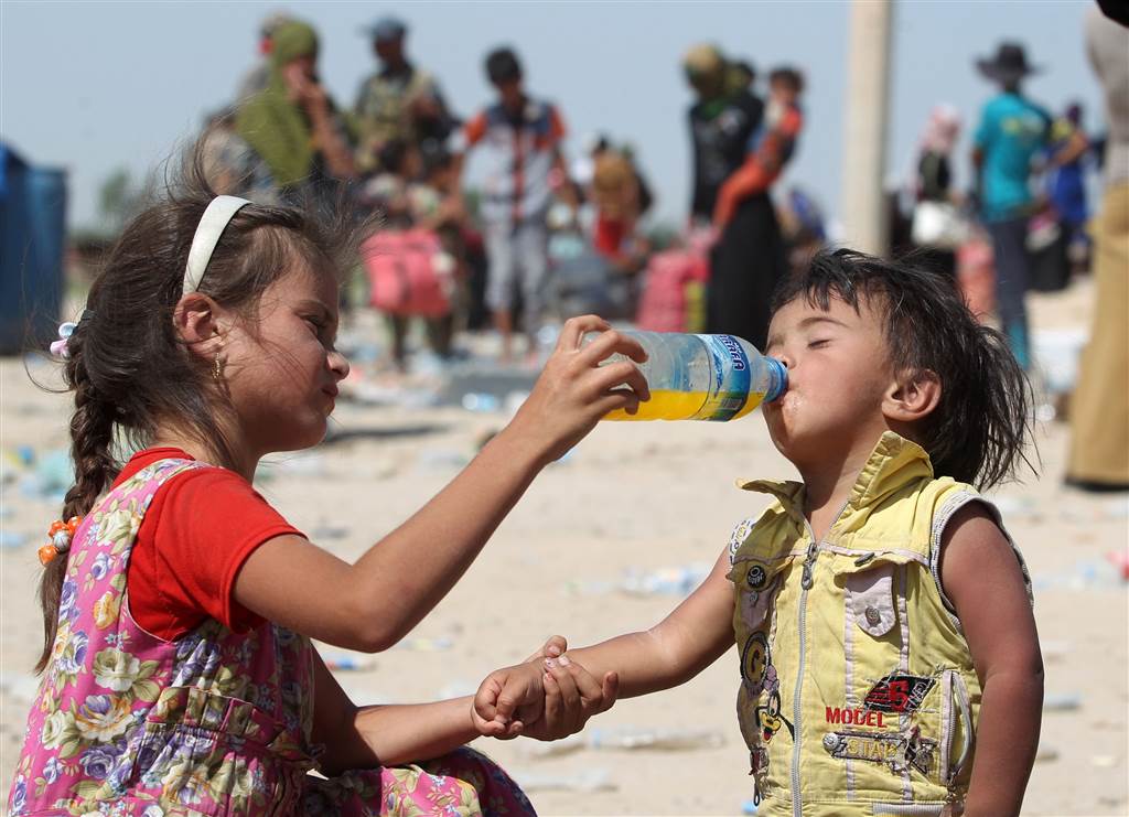 An Iraqi girl helps a young boy drink as they receive food and aid at a military point after fleeing the violence in their village of Saqlawiyah, on June 3
