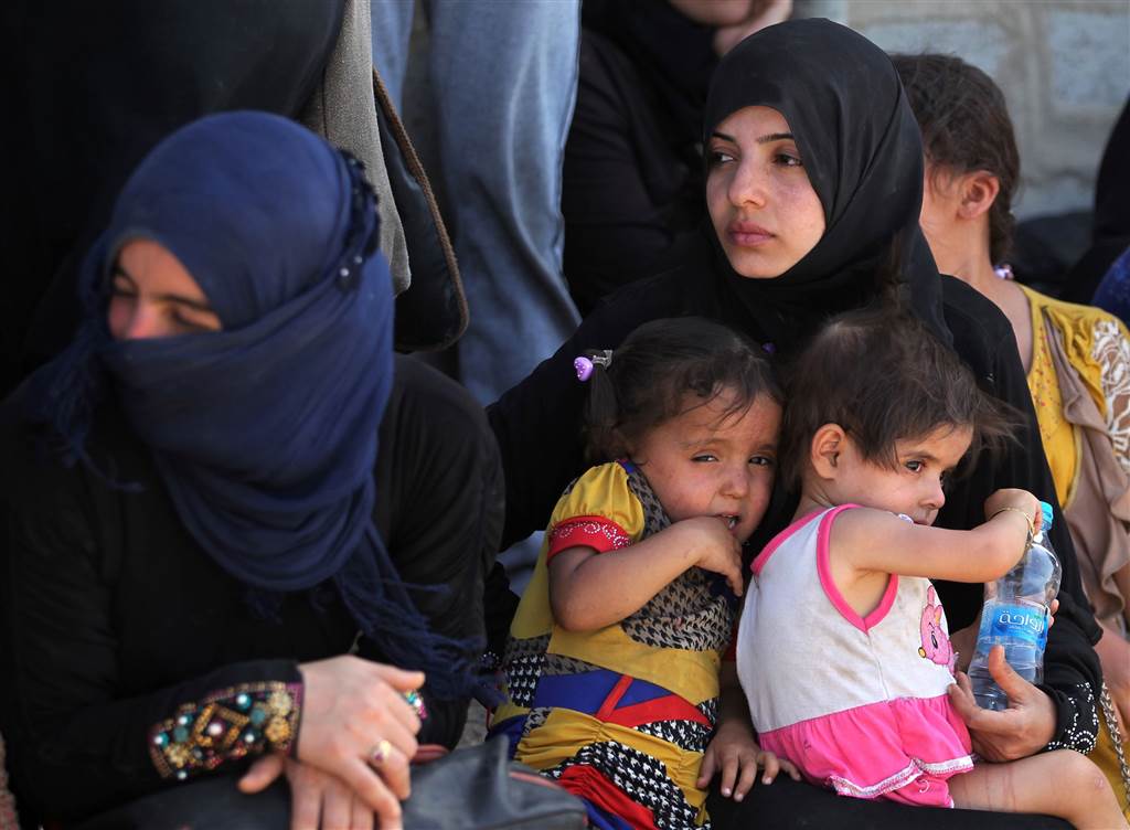 Iraqi women and children who fled the violence in their village of Saqlawiyah wait to receive aid at a military point outside their village, on June 3