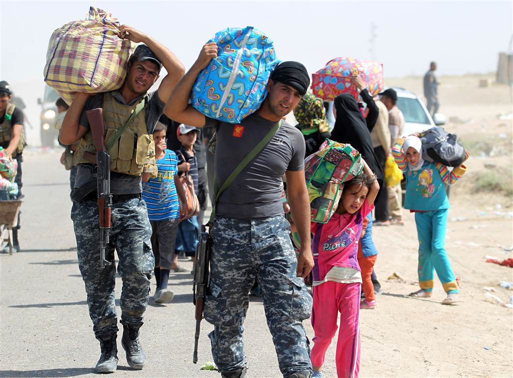Members of the Iraqi government forces help people who fled the violence in Saqlawiyah carry their belongings at a military point outside their village, on June 3